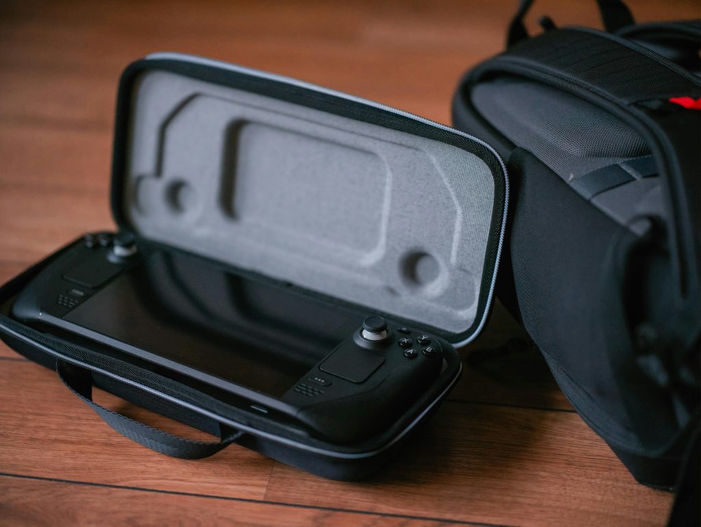 A close-up of a portable gaming device in a protective case next to a bag on a wooden floor.